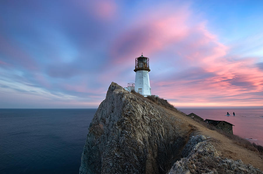 Lighthouse on a high cliff on the coast. Photograph by Vladimir