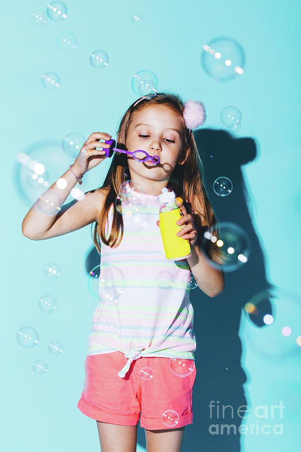 Little girl blowing soap bubbles on a blue background. Photograph by Michal Bednarek