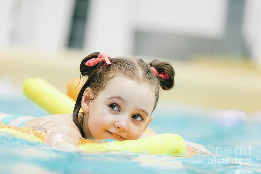 Little girl swimming with a yellow noodle in a pool. Photograph by Michal Bednarek