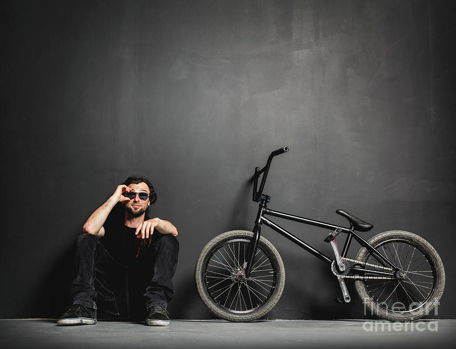 Man sitting next to his BMX bike, adjusting his sunglasses. Photograph by Michal Bednarek