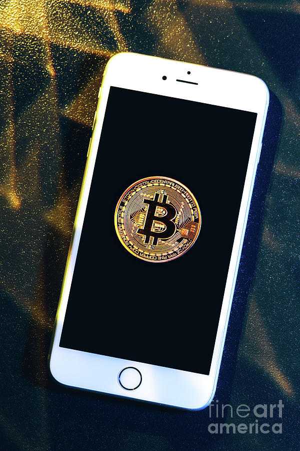 Phone with a bitcoin laying on top of it. Photograph by Michal Bednarek