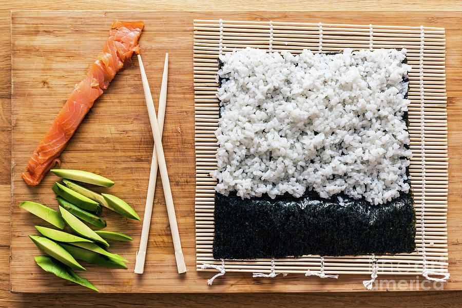 Fish Photograph - Preparing sushi. Salmon, avocado, rice and chopsticks on wooden table by Michal Bednarek