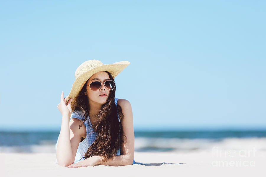 Pretty girl laying on the beach, wearing hat and sunglasses. Photograph by Michal Bednarek