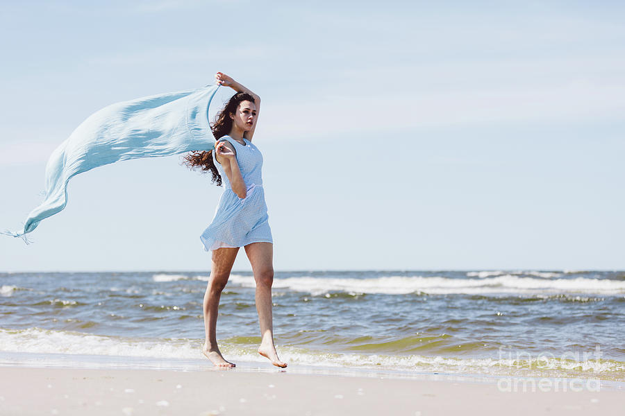 Pretty girl walking by the sea with a blue waving scarf. Photograph by Michal Bednarek