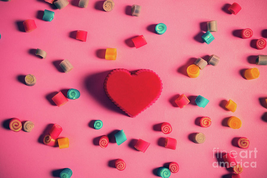 Red heart surrounded by candies on a pink background. Photograph by Michal Bednarek