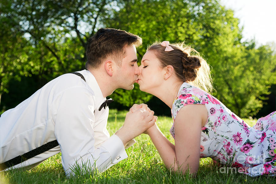 Spring Photograph - Romantic couple in love kissing while lying on grass by Michal Bednarek