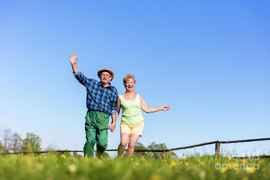 Senior couple holding hands and running outdoors. Photograph by Michal Bednarek