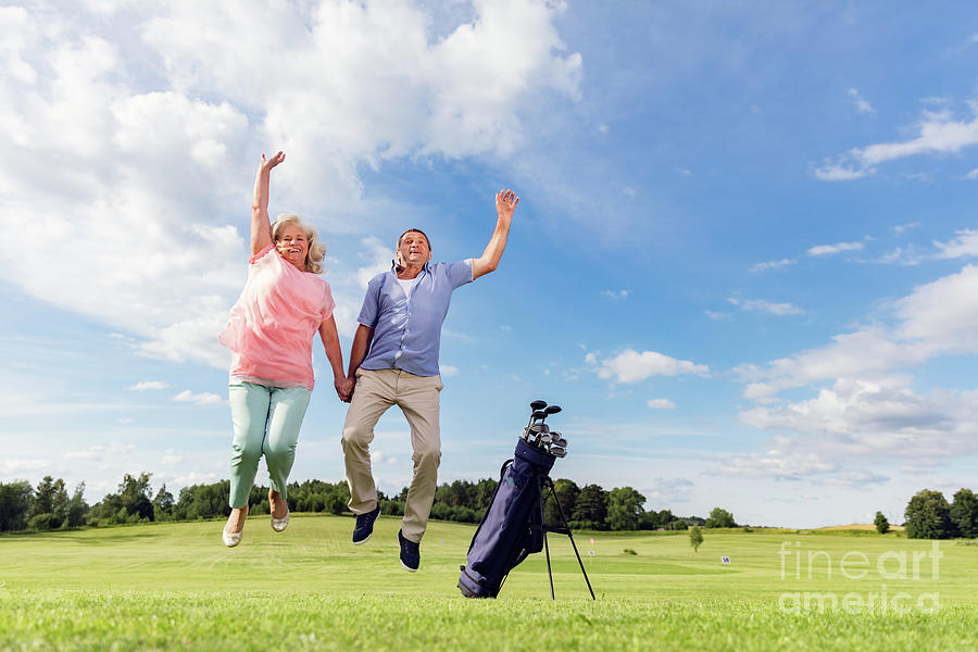 Senior couple jumping on a golf course. Photograph by Michal Bednarek