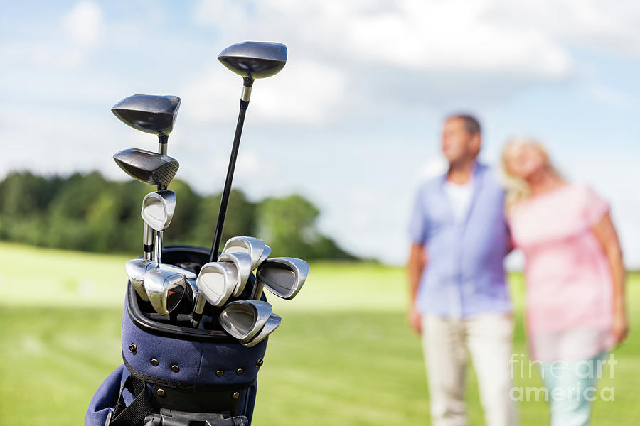 Set of golf clubs with senior couple in the background. Photograph by Michal Bednarek