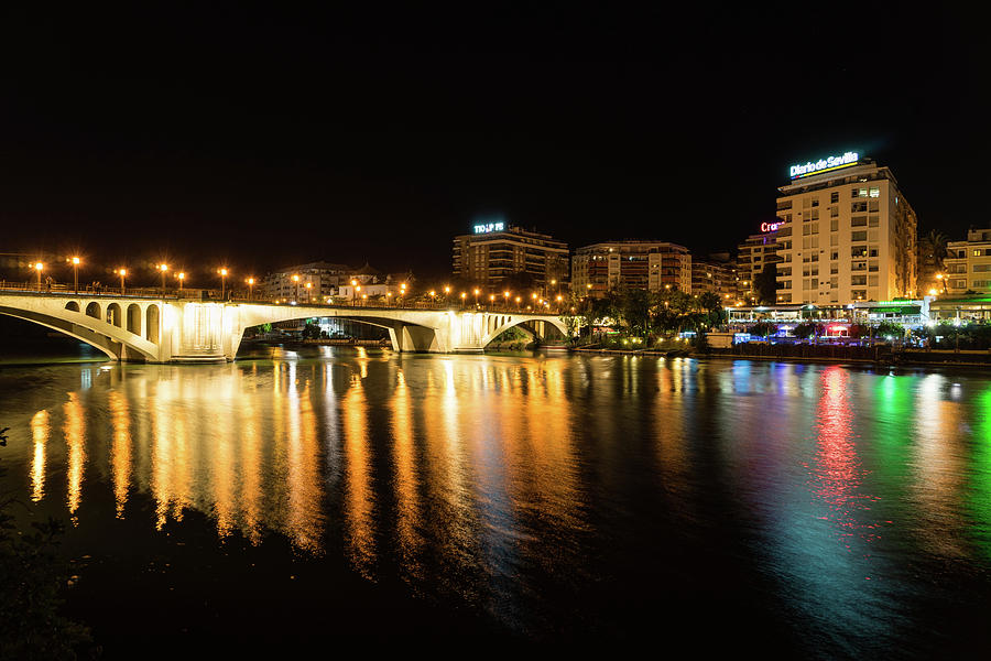 Seville Night Magic - Triana Multicolored Reflections Shimmering in Guadalquivir River Photograph by Georgia Mizuleva