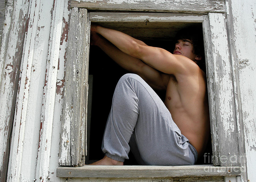 Handsome young man poses seductively in a broken down barn window. Photograph by Gunther Allen