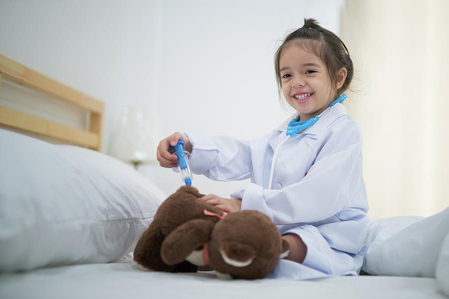 Small girl inject the Teddy Bear by doctor toy set on the bed in Photograph by Anek Suwannaphoom