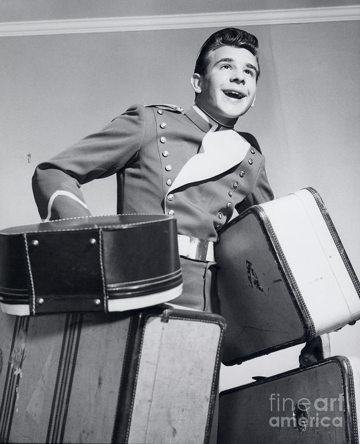 Smiling Bellboy Carrying Luggage Photograph by Debrocke/ClassicStock
