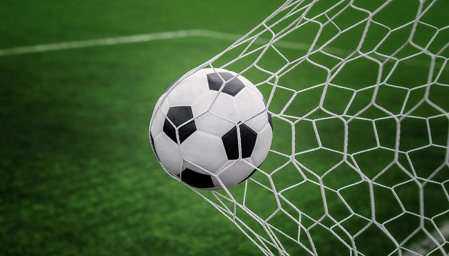 Soccer ball on goal with net and green background Photograph by Anek