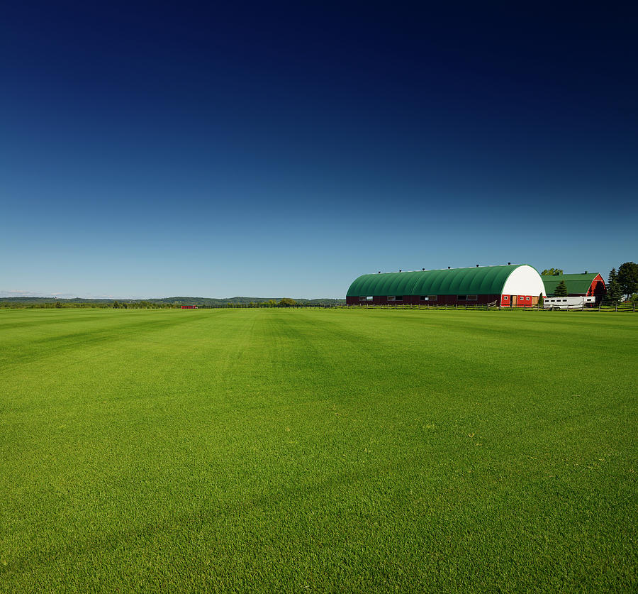 Sod farm field of grass under dark blue sky with large barns in ...