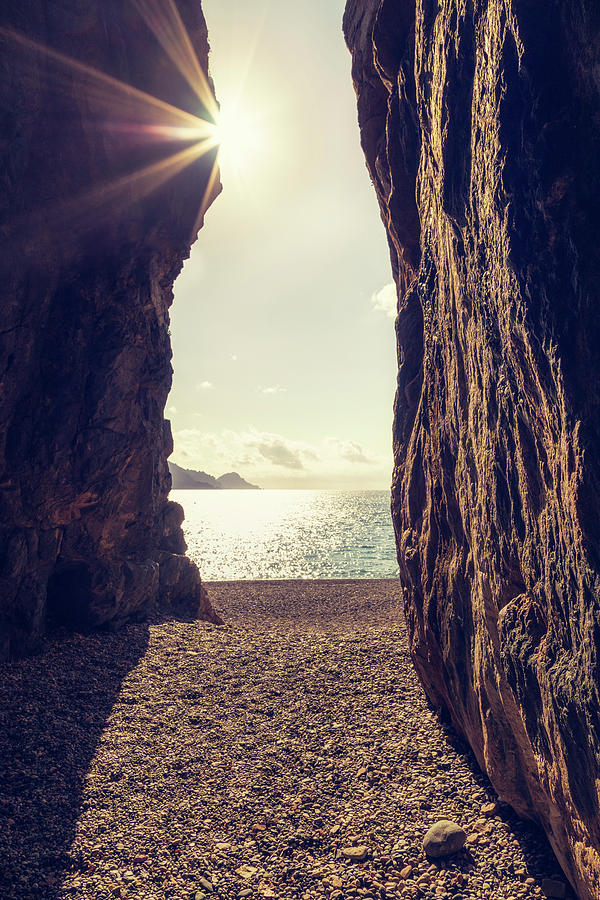 Sunset Photograph - Sun glinting through a cave at Bussaglia beach in Corsica by Jon Ingall