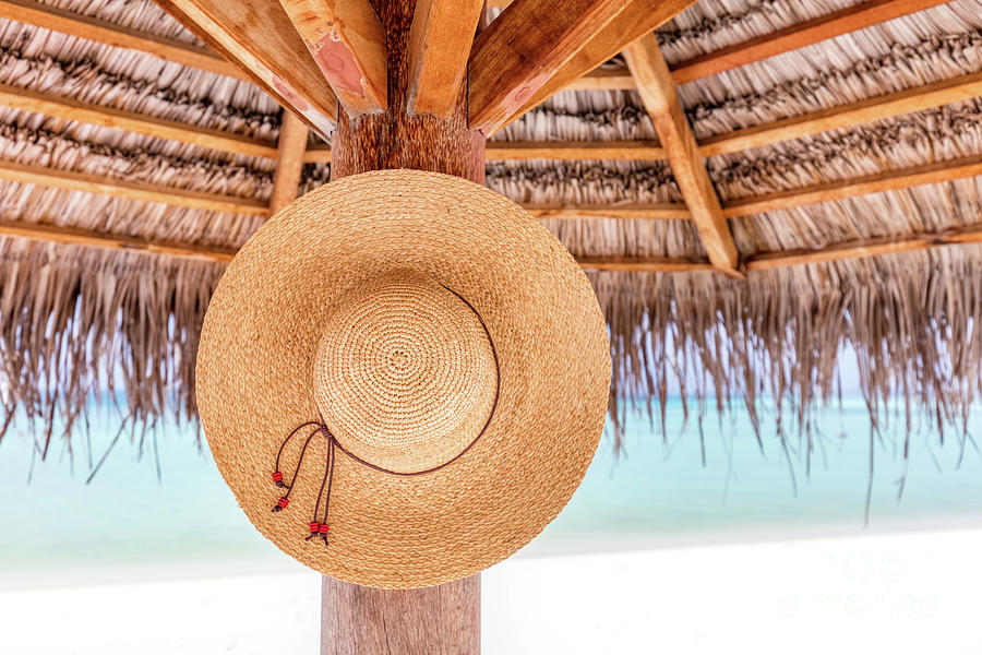 Sun hat hanging on sunshade umbrella on tropical beach. Maldives. Photograph by Michal Bednarek