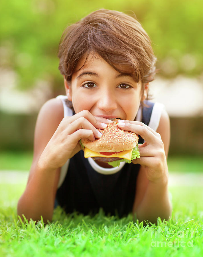 Teen boy eating burger outdoors Photograph by Anna Om