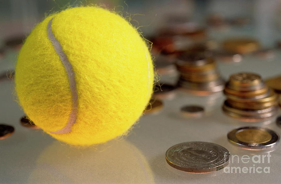 Tennis ball next to numerous piles of coins Photograph by Sami Sarkis
