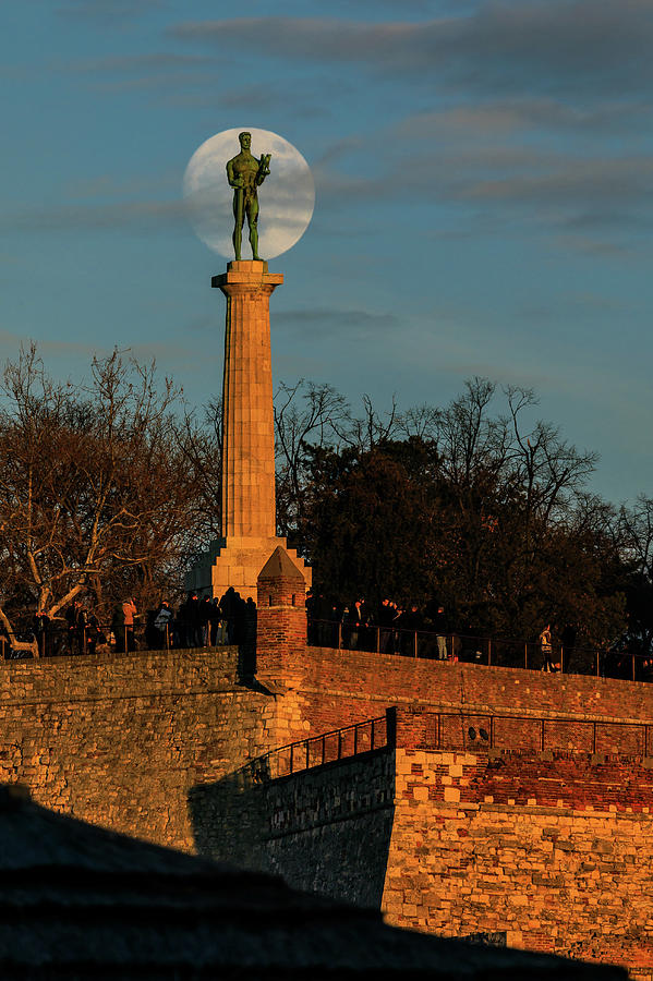 Moon Photograph - The Moon Rising Behind the Victor Statue in Belgrade in the Golden Hour by Dejan Kostic