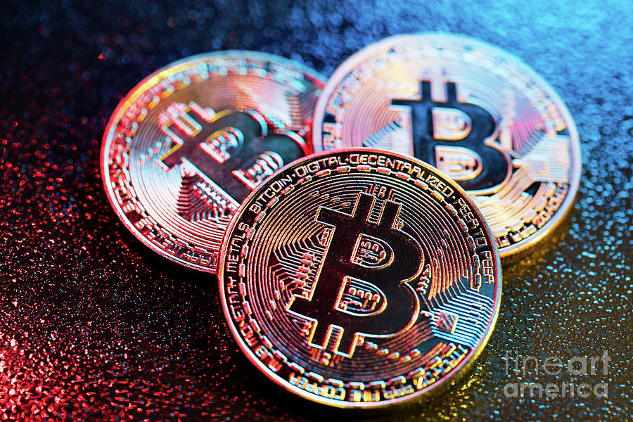 Three bitcoin coins in a colorful lighting. Photograph by Michal Bednarek