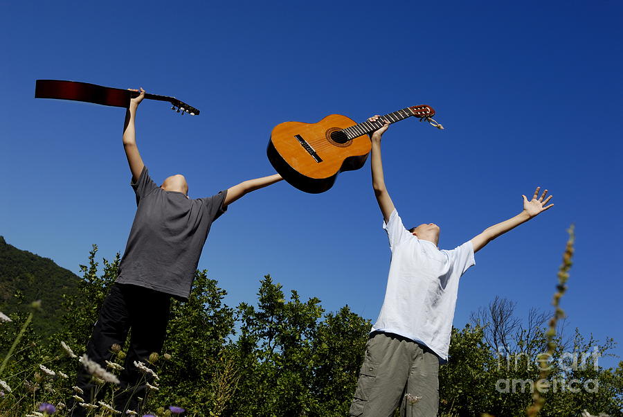 Two boys standing in meadow holding guitars in outstretched arms Photograph by Sami Sarkis