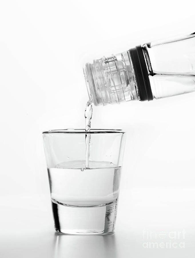 Vodka being poured to a glass. White background. Photograph by Michal Bednarek