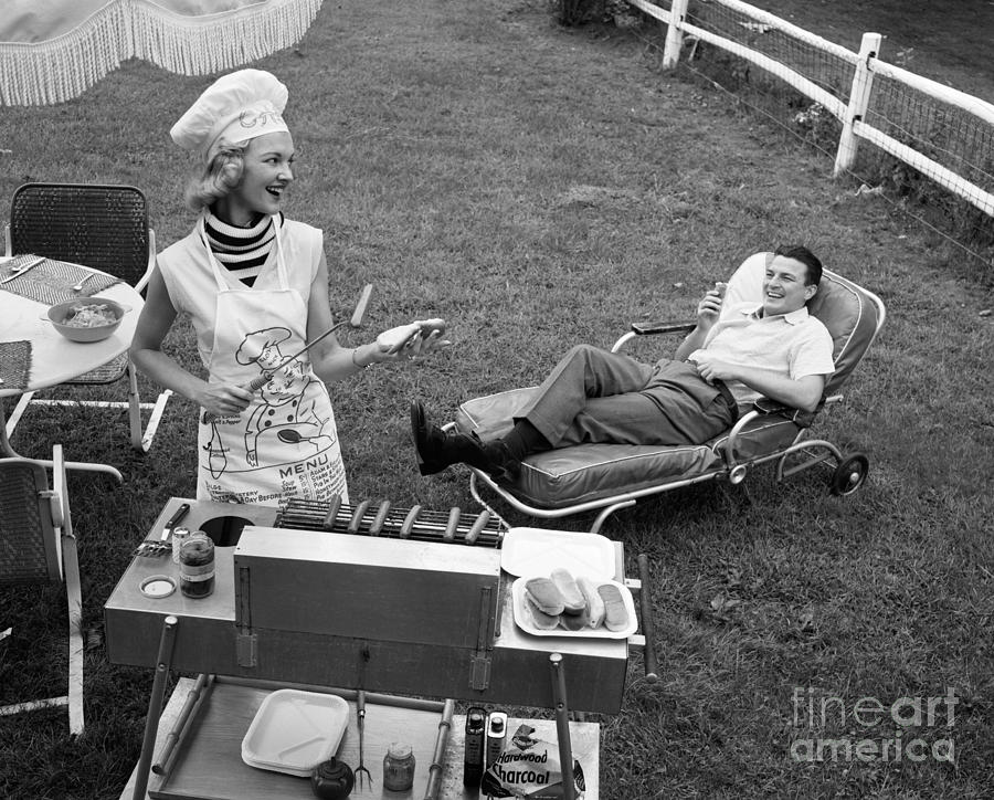 Woman Grilling Hot Dogs For Man Photograph by Debrocke/ClassicStock
