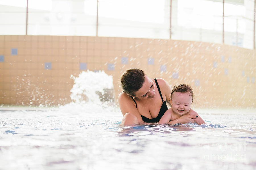 Woman holding sweet baby girl, sitting in a pool. Photograph by Michal Bednarek
