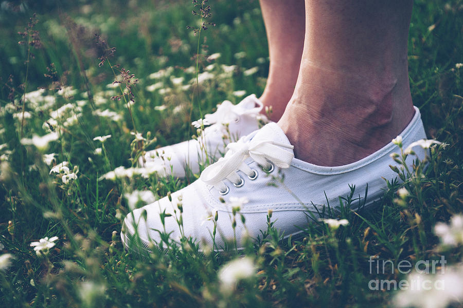 Woman in sneakers standing on meadow with flowers. Photograph by Michal Bednarek