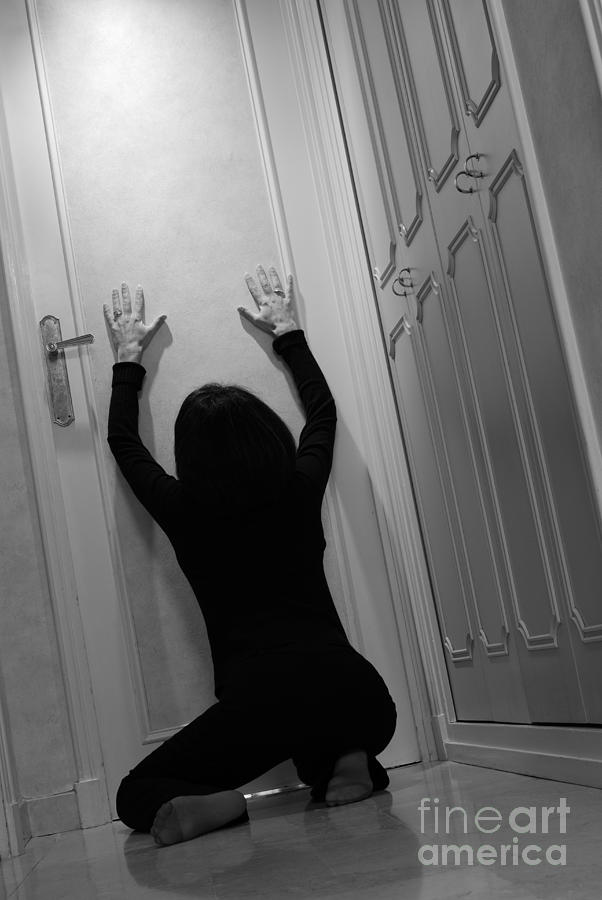 Black And White Photograph - Woman kneeling in corridor with hands on closed door by Sami Sarkis