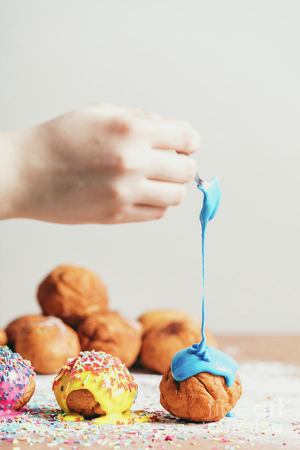 Womans hand coating a doughnut with blue frosting. Photograph by Michal Bednarek