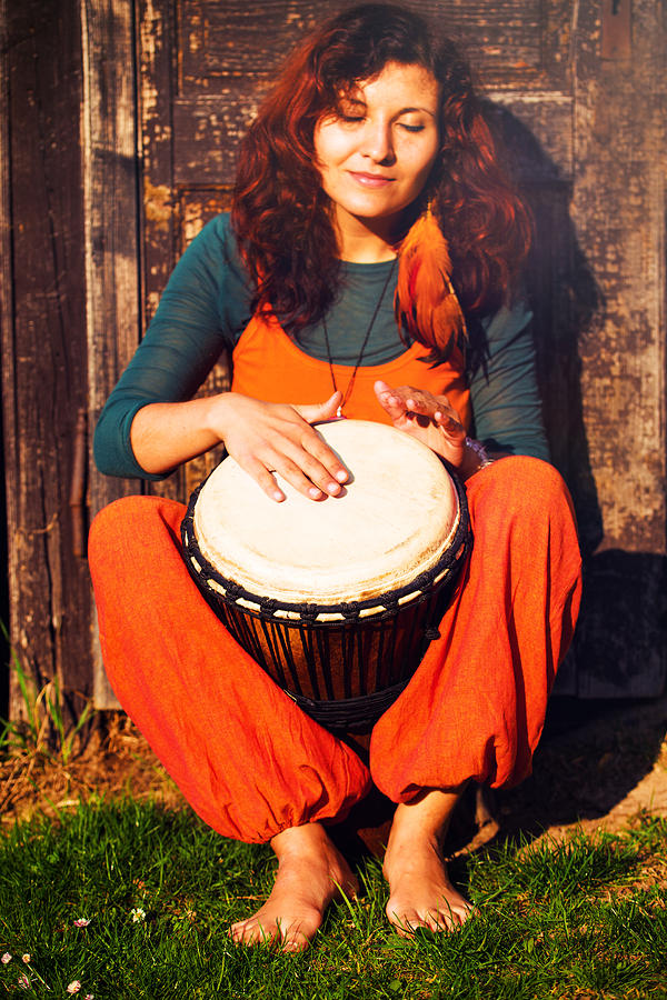 Music Photograph - Young barefoot lady drummer playing on her djembe drum on rustic wooden door background. by Jozef Klopacka