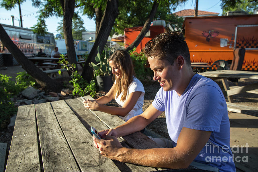 Apple Photograph - Young couple using mobile smart phones plans their evening from an East Austin Food Trailer Park in East Austin by Dan Herron