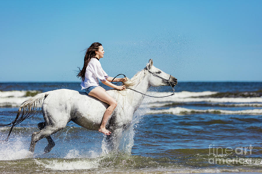 Young girl riding on the white horse through the ocean. Photograph by Michal Bednarek
