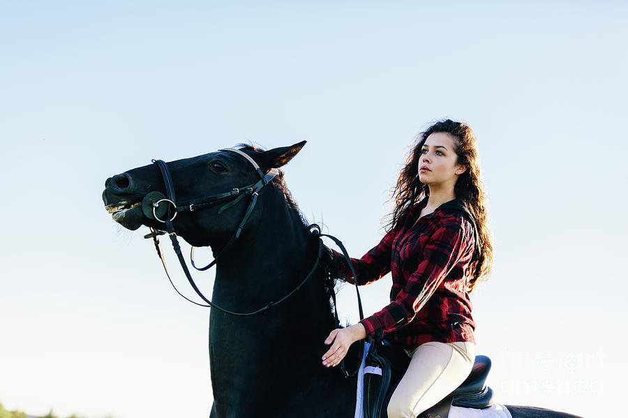 Young girl sitting on a black horse on sky background. Photograph by Michal Bednarek