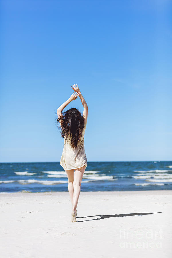 Young girl walking on the beach, holding her hands up. Photograph by Michal Bednarek