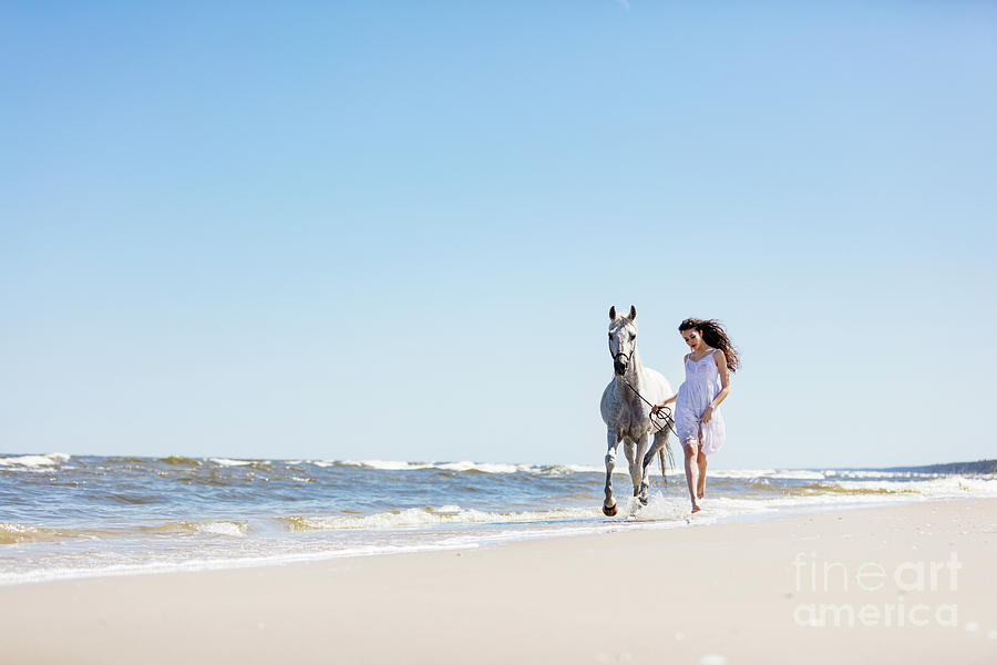 Young girl walking with white horse on the seashore. Photograph by Michal Bednarek