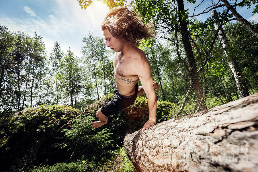 Young Man Jumping Over A Tree Trunk In The Forest. Photograph