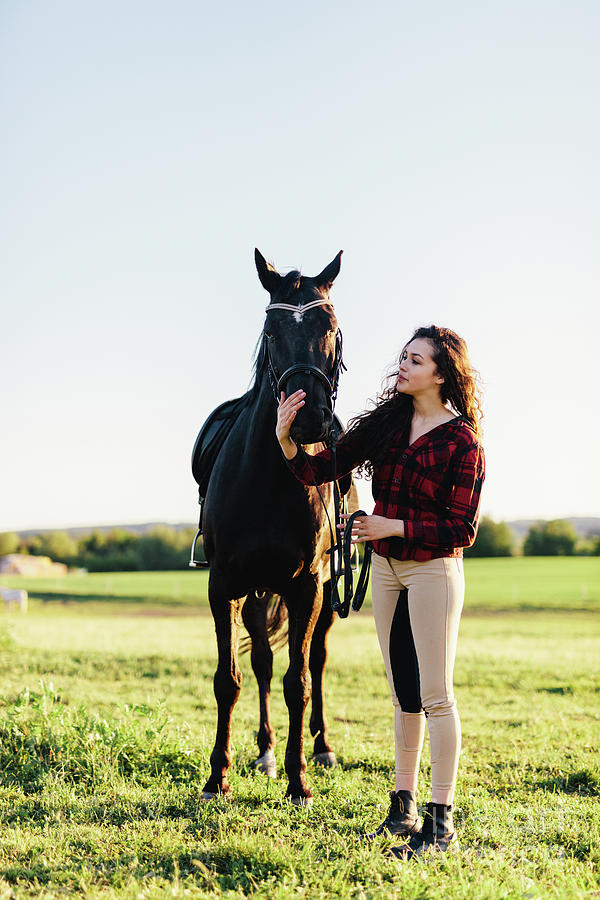 Young woman dressed casually petting black horse Photograph by Michal Bednarek