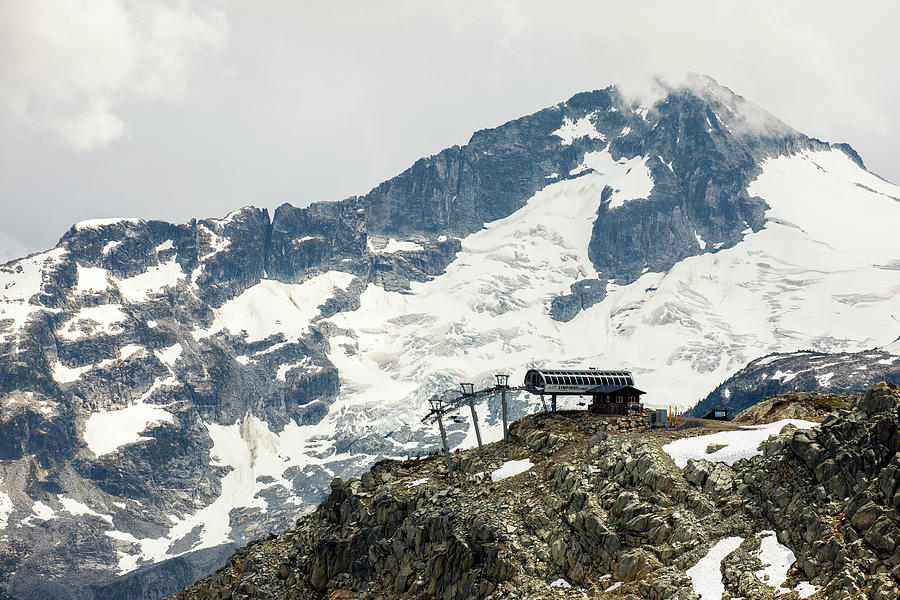 Mountain Photograph - A Chairlift Comes To The Top Of A Mountain Backdropped By A Glaciated Peak Behind In The Coast Mountains Of British Columbia. #1 by Cavan Images