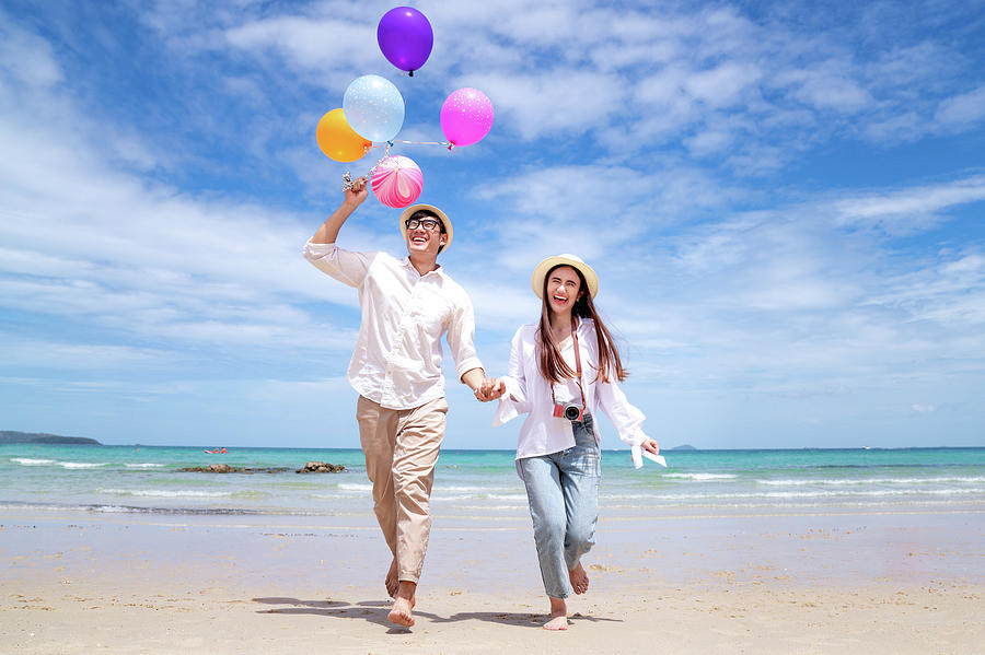 Asian couple run and happy on Pattaya beach with balloon on hand #1 Photograph by Anek Suwannaphoom