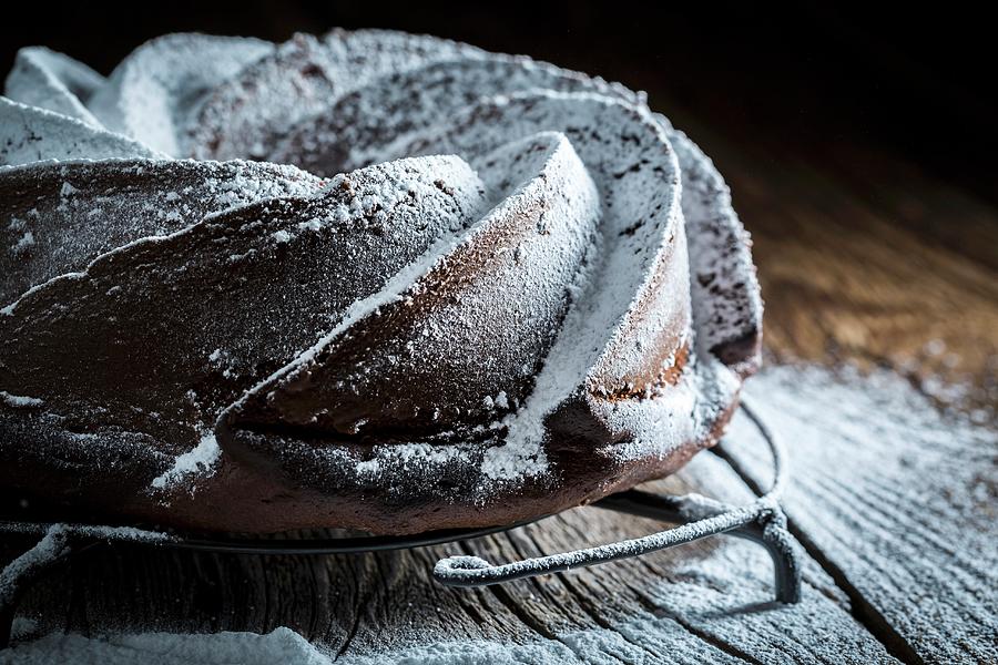 Dark Chocolate Cake Dusted With Icing Sugar On A Wooden Table #1 Photograph by Shaiith