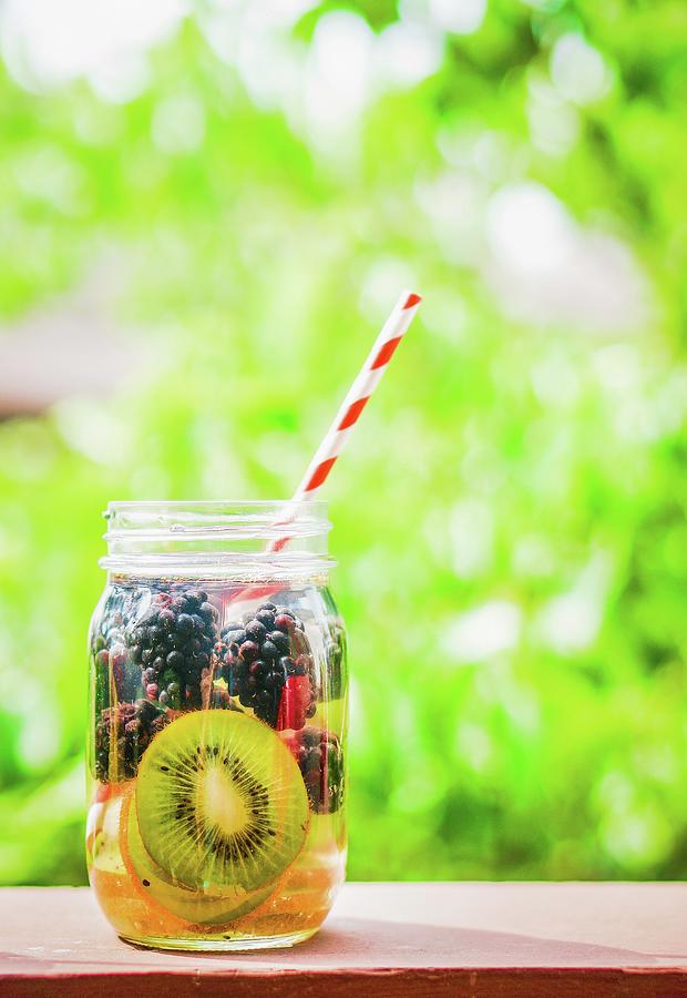 Fruity Iced Tea In A Screw-top Jar With A Straw On A Garden Table #1 Photograph by Alena Haurylik