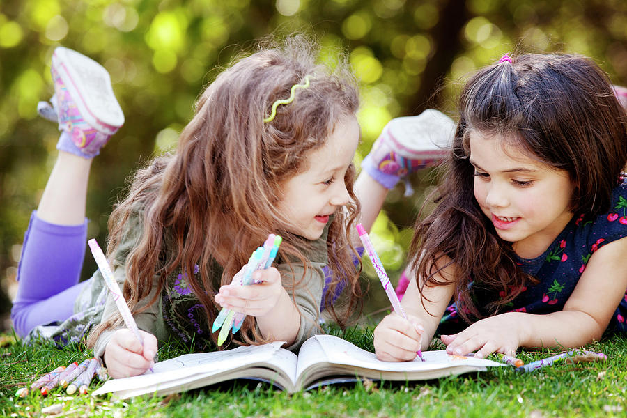 Girls Drawing On Coloring Book While Lying On Field Photograph By Cavan 