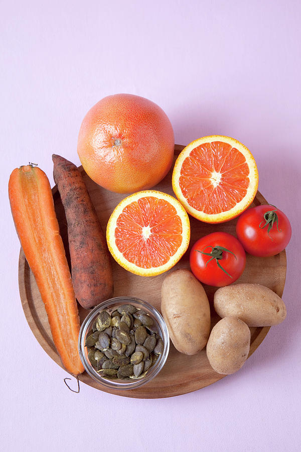 Halved Oranges, Carrots, Tomatoes, Potatoes And Seeds On Pink Background #1 Photograph by Jalag / Annette Falck