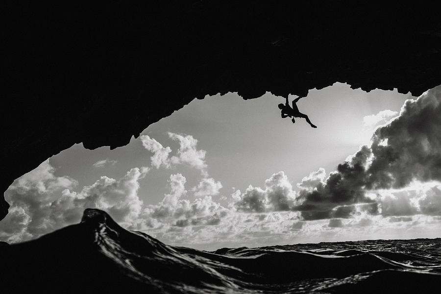 Black And White Photograph - Man Climbing Above The Ocean In A Volcanic Cave #1 by Cavan Images