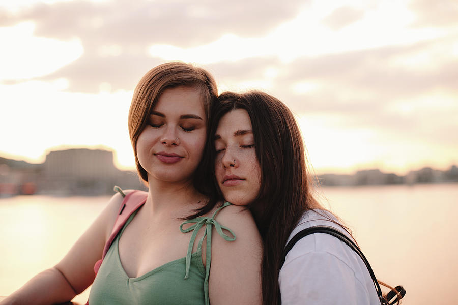 Portrait Of Happy Lesbian Couple Standing On Bridge At Sunset Photograph By Cavan Images