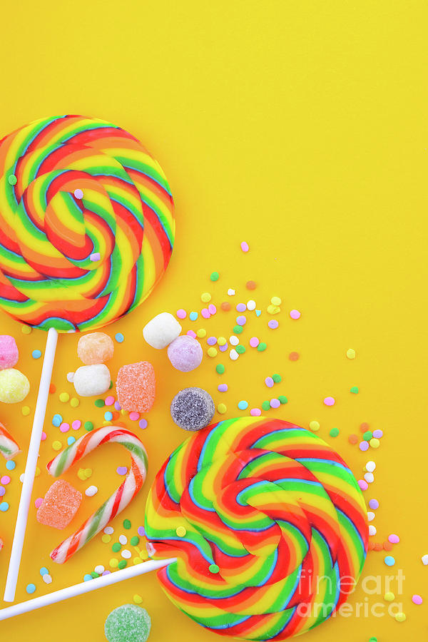 Rainbow lollipop candy on bright yellow wood table.  #1 Photograph by Milleflore Images