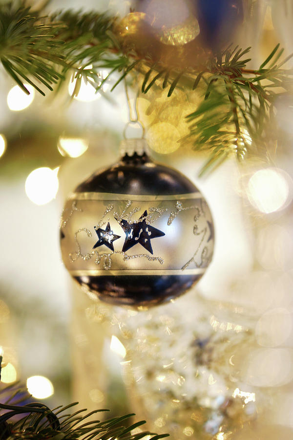 Silver-and-blue Christmas Bauble Hung From Branch In Front Of Sparkling Lights #1 Photograph by Angelica Linnhoff